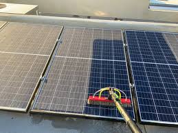Rooftop solar panels being cleaned with a long-handled brush, one panel already clean
